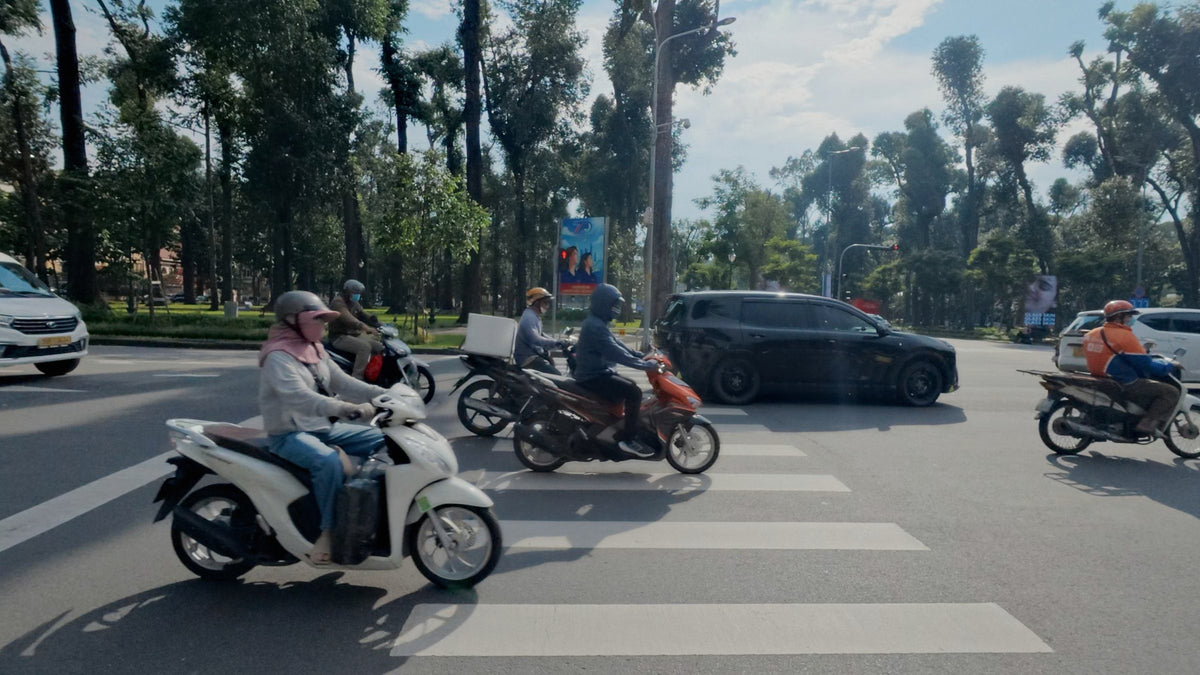 Motorbikes crossing a tree-lined street in Ho Chi Minh City